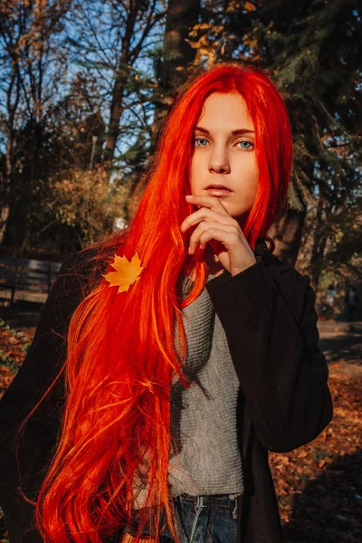 Sexy beautiful redhead girl with long, strong and thick hair. Perfect woman portrait on a background of autumn foliage. Gorgeous deep blue eyes. Natural beauty, clean skin, face and hair care.