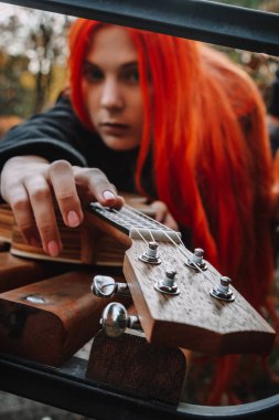 Kızıl saçlı, uzun saçlı kız parkta ukulele çalıyor. Okul, müzik eğitimi konsepti, öğrenci telli çalgılar çalmayı öğreniyor. Bir müzisyenin elleri, klasik, melodi, yaratıcılık.
