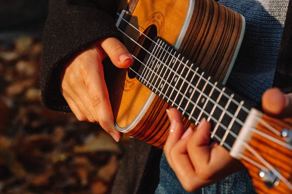 Rudowłosa dziewczyna z długimi włosami bawi się na ukulele w parku. Szkoła, koncepcja edukacji muzycznej, student uczy się grać na instrumencie smyczkowym. Dłonie muzyka, klasyka, melodia, kreatywność. — Zdjęcie stockowe