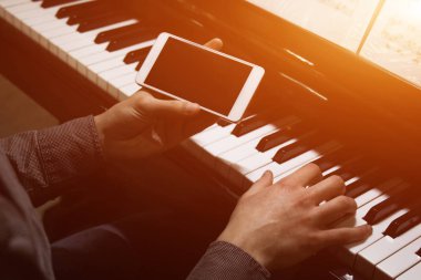 İki erkek eli piyanonun üzerinde, akıllı telefonlu. Avuçlar tuşlara uzanır ve müzik okulunda klavye çalar. Öğrenci çalmayı öğreniyor. Bir piyanistin elleri. siyah arkaplan.
