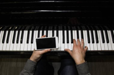 two male hands on the piano with a smartphone. palms lie on the keys and play the keyboard instrument in a music school. student learns to play. hands of a pianist. black dark background. clipart