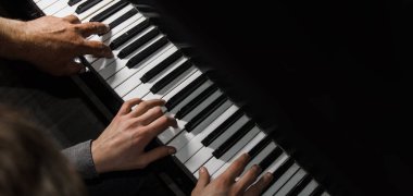 Piyanoda dört erkek eli oynuyordu. Avuçlar tuşlara uzanır ve müzik okulunda klavye çalar. Öğrenci çalmayı öğreniyor. Bir piyanistin elleri. siyah arkaplan.