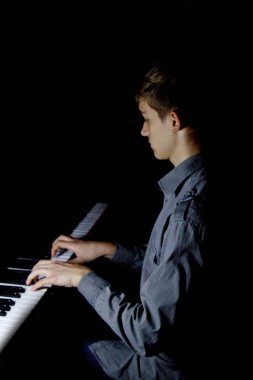 Genç adam piyanonun başında oturuyor. Erkek çocuk müzik okulunda klavye enstrümanı çalıyor. Öğrenci çalmayı öğreniyor. Eller piyanist. Siyah siyah arka plan. dikey.
