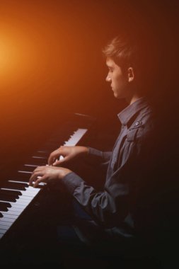 Genç adam piyanonun başında oturuyor. Erkek çocuk müzik okulunda klavye enstrümanı çalıyor. Öğrenci çalmayı öğreniyor. Eller piyanist. Siyah siyah arka plan. dikey.