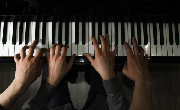 Grając na fortepianie czterema męskimi rękami. dłonie leżą na klawiszach i grają na instrumencie klawiszowym w szkole muzycznej. Uczeń uczy się grać. Ręce pianisty. czarne ciemne tło. — Zdjęcie stockowe