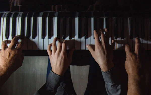 Tocando cuatro manos masculinas en el piano. las palmas yacen en las teclas y tocan el instrumento de teclado en una escuela de música. estudiante aprende a jugar. manos de un pianista. fondo negro oscuro . — Foto de Stock