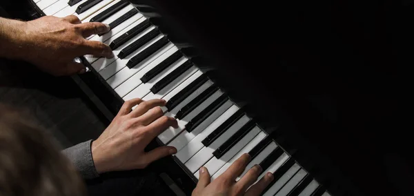 Jouer quatre mains masculines sur le piano. palms se trouvent sur les touches et jouent de l'instrument à clavier dans une école de musique. élève apprend à jouer. les mains d'un pianiste. fond noir foncé . — Photo