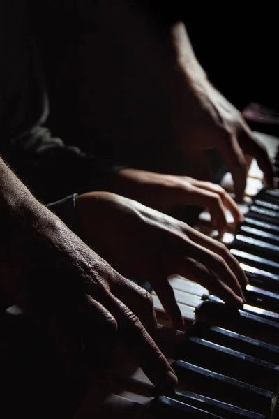 ピアノで4人の男性の手を演奏しましたヤシは鍵の上に横たわり音楽学校で鍵盤楽器を演奏します生徒は遊ぶことを学ぶピアニストの手だ黒い闇の背景. — ストック写真