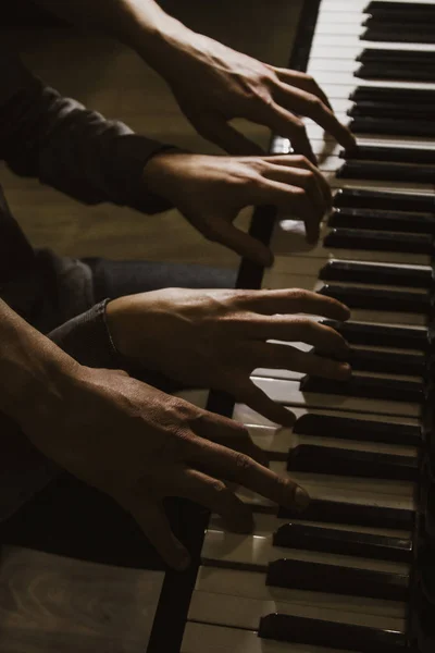 Vier mannelijke handen spelen op de piano. palmen liggen op de toetsen en bespelen het keyboard instrument in een muziekschool. student leert spelen. handen van een pianist. zwarte donkere achtergrond. — Stockfoto