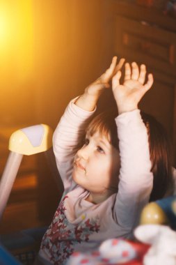 Bir yaşında gülümseyen bir kız yüksek bir sandalyede çocuk masasında oturur ve bir kaşıkla yemek yer. Renkli arka plan. Çocuklar için sağlıklı beslenme. Bebek maması..