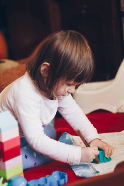 Bir yaşındaki gülümseyen kız kalemle resim çiziyor. Renkli arka plan. Çocuklar için geliştirme oyunları. Yaratıcı eğlence.