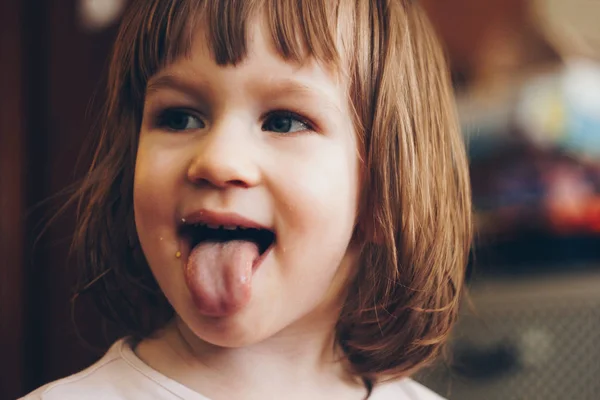 A one-year-old smiling girl sits at a children's table in a high chair and eats with a spoon from a bowl. Colored background. Healthy eating for kids. Baby food. — Stock Photo, Image