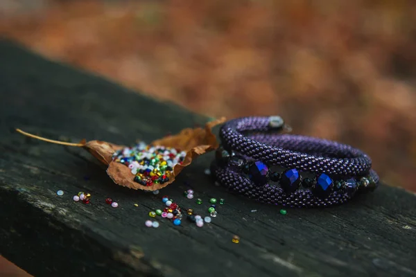 Beautiful, shiny, color bracelet with large beadwork beads. On a special stand for jewelry. Beads are scattered on a wooden table. — Stock Photo, Image