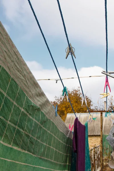 En klädnypa hänger på tvättlina. Ett rep med rena linne och kläder utomhus på tvättdagen. Mot bakgrund av grön natur och himmel. — Stockfoto