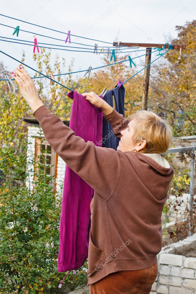 Laundry woman hangs clean wet cloth on clothes dryer after washing at home. Household chores and housekeeping.