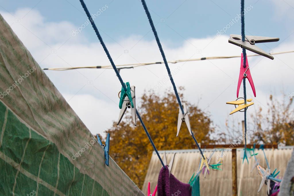 A clothespin hangs on the washing line. A rope with clean linen and clothes outdoors on the day of the laundry. Against the background of green nature and sky.