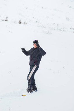 Snowboard yapan mutlu genç adam karlı dağlarda güneşli havanın tadını çıkarıyor. Kış sporu ve eğlence, açık hava aktiviteleri..