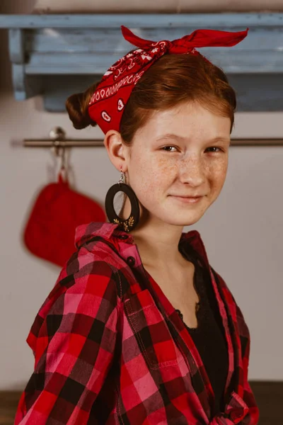 Aranyos vörös hajú lány szeplőkkel, piros kendőben és kockás ingben a konyha hátterében. Reklám, pin-up fotó koncepció. — Stock Fotó