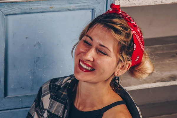 Retrato de uma menina sorridente deslumbrante com lábios vermelhos, vestida com uma camisa vermelha quadriculada e uma bandana na cabeça. Modelo posando em estilo de moda retro e conceito vintage . — Fotografia de Stock