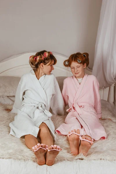 Happy loving family. Mom and daughter do manicures, pedicures, do makeup and have fun. Mom and little girl in bathrobes and with curlers on their heads.