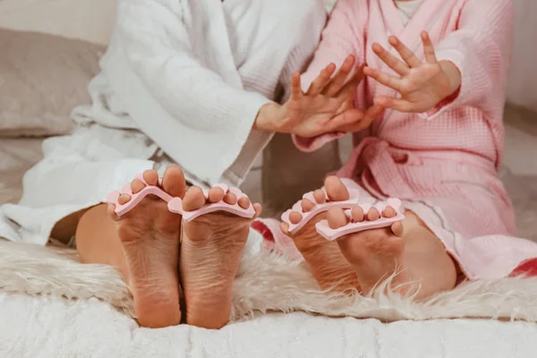 Glückliche liebende Familie. Mutter und Tochter machen Maniküre, Pediküre, machen Make-up und haben Spaß. Mutter und kleines Mädchen in Bademänteln und mit Lockenwicklern auf dem Kopf. — Stockfoto