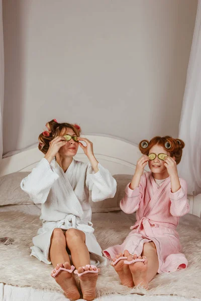 Holiday day at home. Mom and daughter at home make a mask of cucumber on the eyes. Beauty Salon Concept. Beautiful face. Woman and happy baby. Girls with curlers.