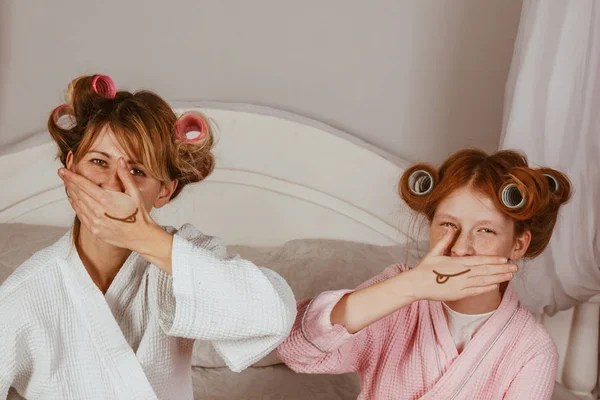 Anya és lánya otthon uborkát készítenek. Szemeket a kezekre. Szépségszalon koncepció. Gyönyörű arc. Nő és boldog baba. Lányok hajcsavaróval. — Stock Fotó