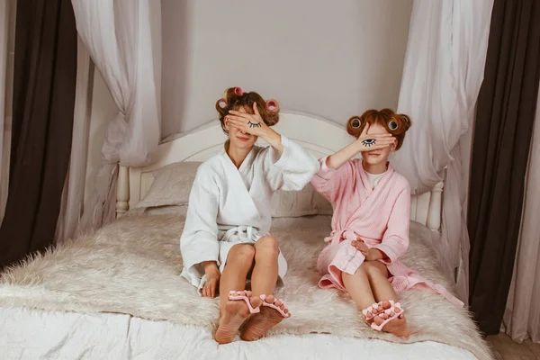 Mãe e filha em casa fazem uma máscara de pepino. Olhos desenhados nas mãos. Conceito de salão de beleza. Lindo rosto. Mulher e bebé feliz. Meninas com encrespadores . — Fotografia de Stock