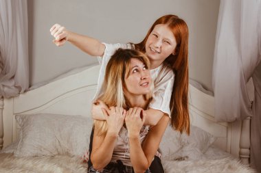 Anneler Günün kutlu olsun. Anne ve kızı yatakta kız gibi gülüp sarılıyorlar. Aile tatilleri ve birliktelik.