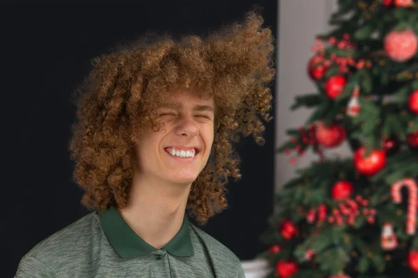Celebration, people and holidays concept - happy curly guy while Christmas or New Year party on the background of a beautiful Christmas tree. — Stock Photo, Image