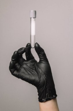 Empty test tube in a glass flask in the hands of a scientist or cosmetologist. Black gloves on a gray background. Experiment, analyzes, girl from the back.