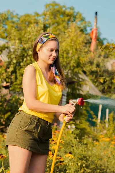 Prachtige jonge glimlachende vrouw die planten water geeft in haar tuin met een tuinslang. hobbyconcept. — Stockfoto