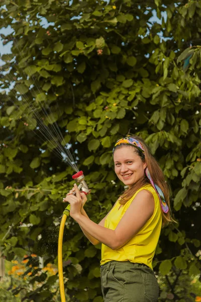 Summer garden, watering - beautiful girl watering roses with garden hose in the garden.