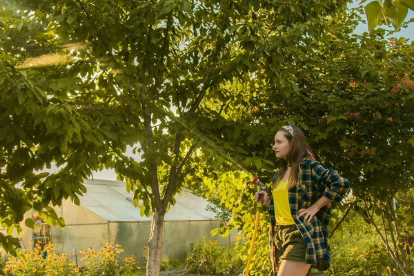 Jovem menina bonita se divertindo no jardim regando plantas com uma mangueira. Sorrindo enquanto toma um hobby favorito . — Fotografia de Stock