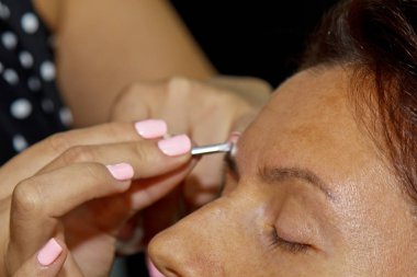 Usta makyajı ayarlar ve daha önce bir güzellik salonunda kınalı kaşlarla boyanmış olan forseps ile çıkartmak için form verir. Profesyonel yüz bakımı.