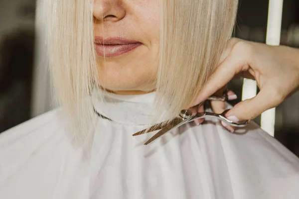 Closeup of a hairdresser cuts wet white hair of a client in a salon. Hairdresser cuts a woman. Side view of a hand cutting hair with scissors. — Stock Photo, Image