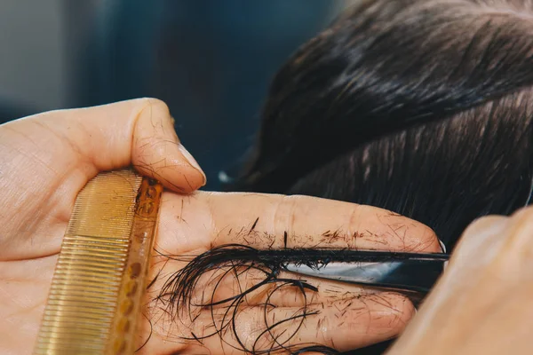 O fim de um cabeleireiro corta o cabelo marrom molhado de um cliente em um salão. O cabeleireiro corta uma mulher. Vista lateral de um cabelo de corte de mão com tesoura . — Fotografia de Stock