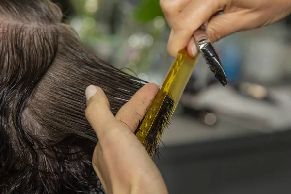 O fim de um cabeleireiro corta o cabelo marrom molhado de um cliente em um salão. O cabeleireiro corta uma mulher. Vista lateral de um cabelo de corte de mão com tesoura . — Fotografia de Stock