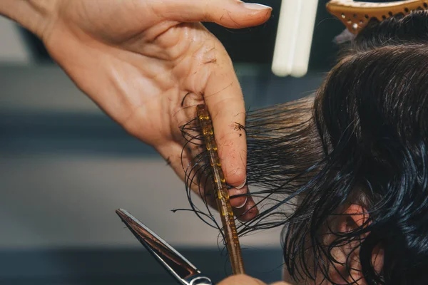 O fim de um cabeleireiro corta o cabelo marrom molhado de um cliente em um salão. O cabeleireiro corta uma mulher. Vista lateral de um cabelo de corte de mão com tesoura . — Fotografia de Stock