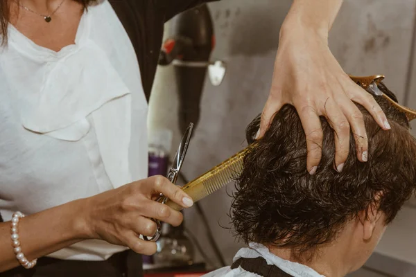 O fim de um cabeleireiro corta o cabelo marrom molhado de um cliente em um salão. O cabeleireiro corta uma mulher. Vista lateral de um cabelo de corte de mão com tesoura . — Fotografia de Stock