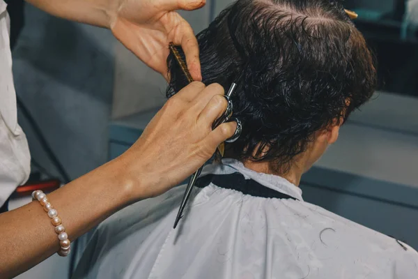 O fim de um cabeleireiro corta o cabelo marrom molhado de um cliente em um salão. O cabeleireiro corta uma mulher. Vista lateral de um cabelo de corte de mão com tesoura . — Fotografia de Stock