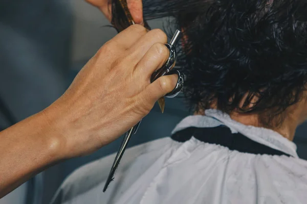 O fim de um cabeleireiro corta o cabelo marrom molhado de um cliente em um salão. O cabeleireiro corta uma mulher. Vista lateral de um cabelo de corte de mão com tesoura . — Fotografia de Stock