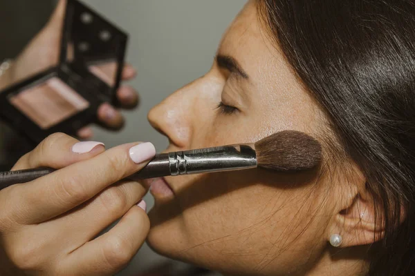 Dziewczyna maluje proszek na twarzy, uzupełnia smokey makijaż oczu w salonie piękności. Profesjonalna pielęgnacja skóry. — Zdjęcie stockowe