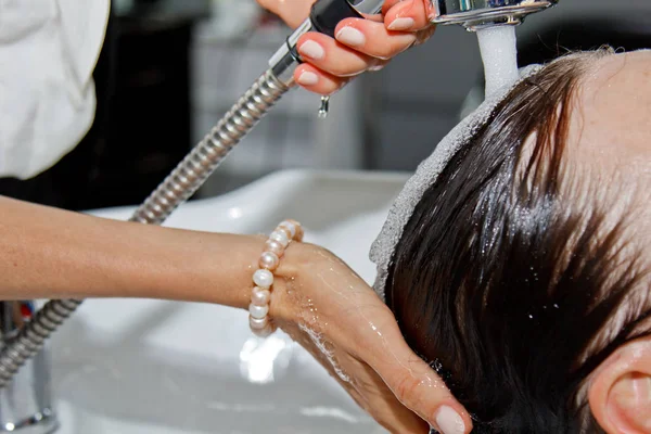 Linda mulher idosa alegre goza de uma massagem na cabeça enquanto lava o cabelo por um cabeleireiro profissional. Cuidados de beleza, penteado, moda, estilo de vida conceito glamour. Gotas de água e espuma de xampu . — Fotografia de Stock