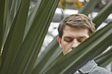 Depresyondaki yakışıklı adam. Botanik bahçesinde kafasını tutan tıraşlı bir hipster değil. Kavram: baş ağrısı ve keder.