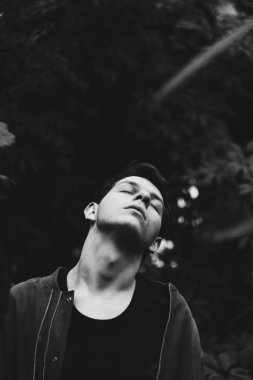 Yeşil yapraklı genç bir adamın portresi. İyi bir adam yeşil bitkilerden oluşan bir duvara karşı duruyor. Sarmaşık çalılıkları içinde beyaz bir adamın yakın çekim.