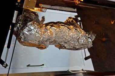 Prag 'da. 05.10.2019: Et pişirme sürecinde büyük bir barbekü, mutfaktaki bir restoranda kömür pişirmek için gıda folyosuna sarılmış bir domuz yavrusu. Vejetaryenlik kavramı.