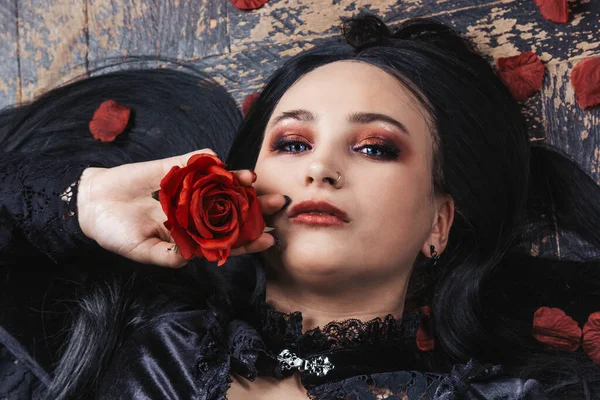 Siyah elbiseli, uzun saçlı, mutlu, büyük beden bir manken ahşap bir zeminde yatıyor. Kameraya gül yapraklarıyla poz veren tombul bir kadın. Vücut pozitif. Tek bir güzellik kavramı. Xxxl modası