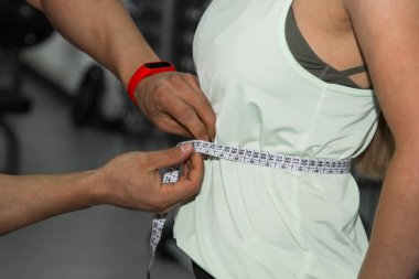 Kilo kaybı, kişisel antrenör, beslenme uzmanı, fitness, motivasyon, sağlıklı yaşam tarzı. Bir erkek, bir kızın belini mezurayla ölçer. Yaklaş, makro fotoğraf. Eğitim için hazırlama