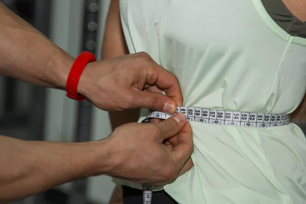 パーソナルトレーナー 栄養士 フィットネス 動機づけ 健康的なライフスタイル 男は測定テープで女の子の腰を測定します 閉じて マクロ写真 訓練の準備 — ストック写真